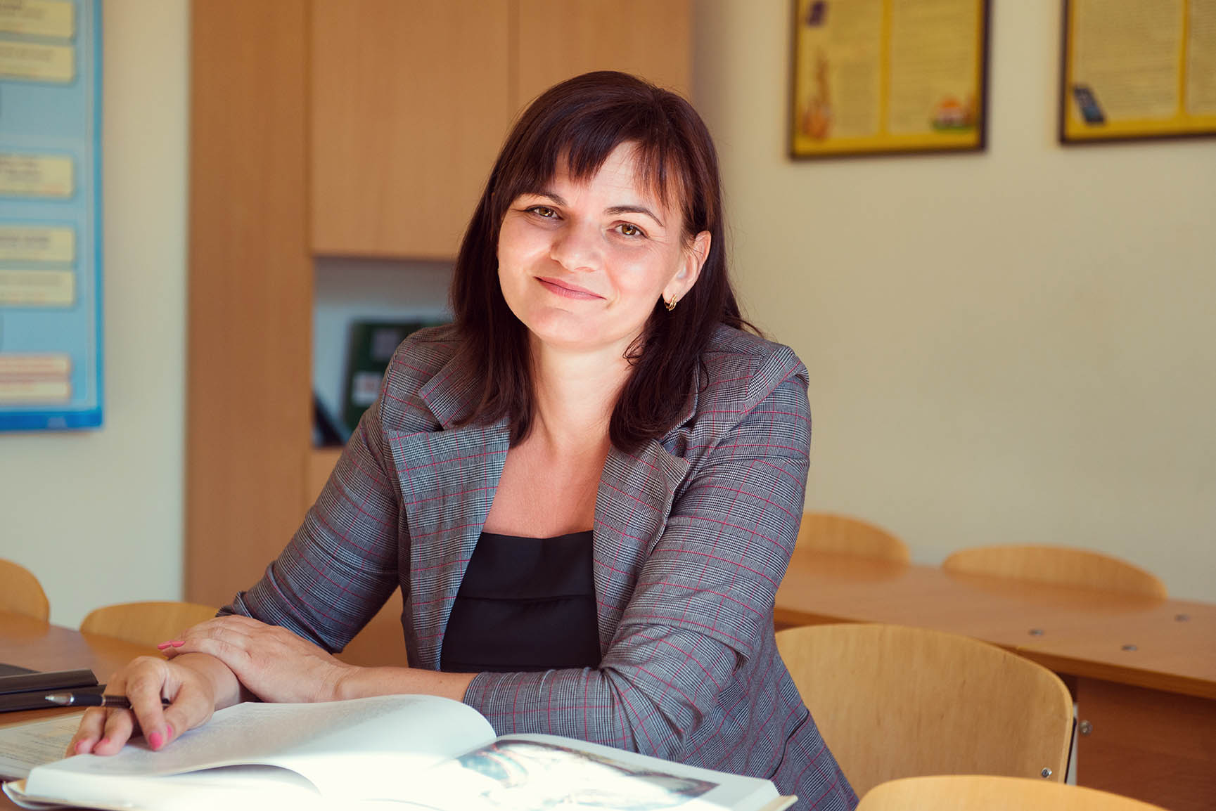 Teacher smiling while seated at a classroom table.