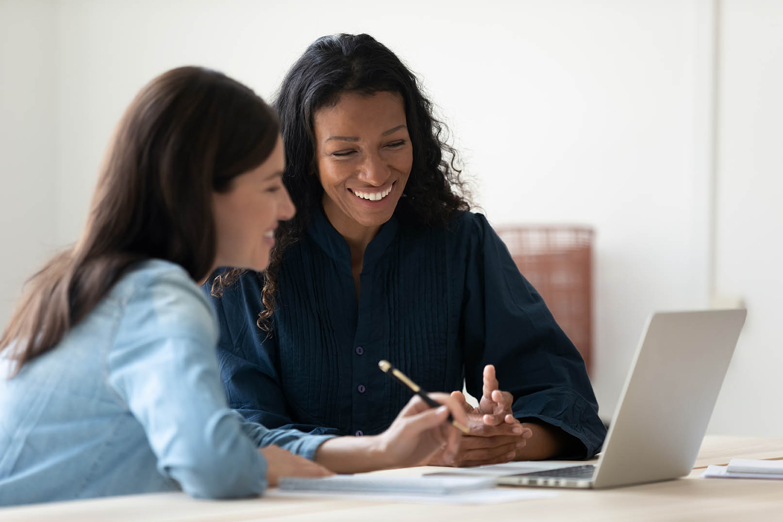 Two people collaborating at a desk, reviewing notes and working on a laptop together.