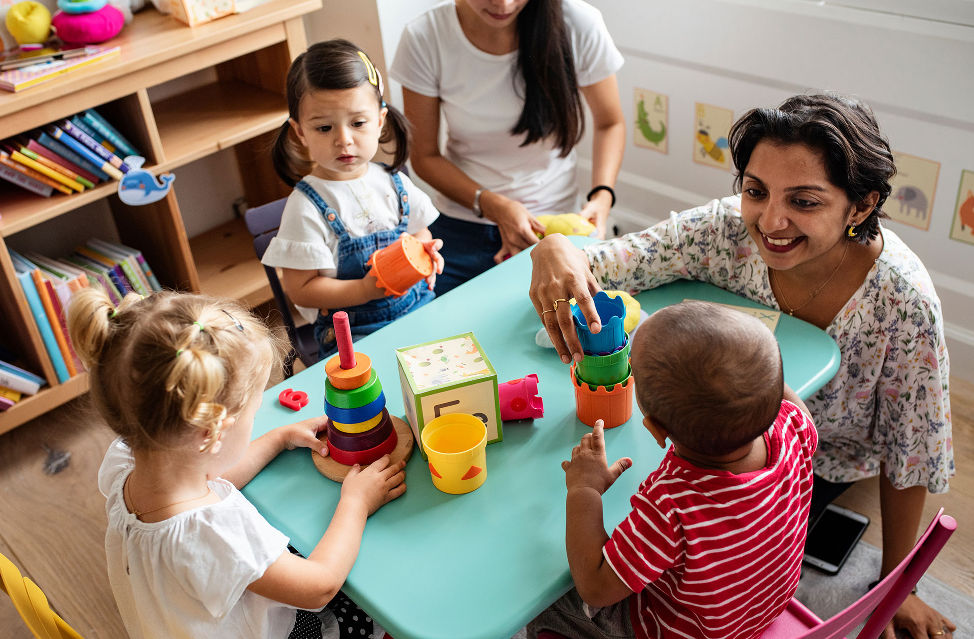 Early childhood teacher playing with toddlers at a classroom table.