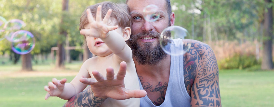 "Adult and young child reaching for bubbles while playing outdoors in a park."